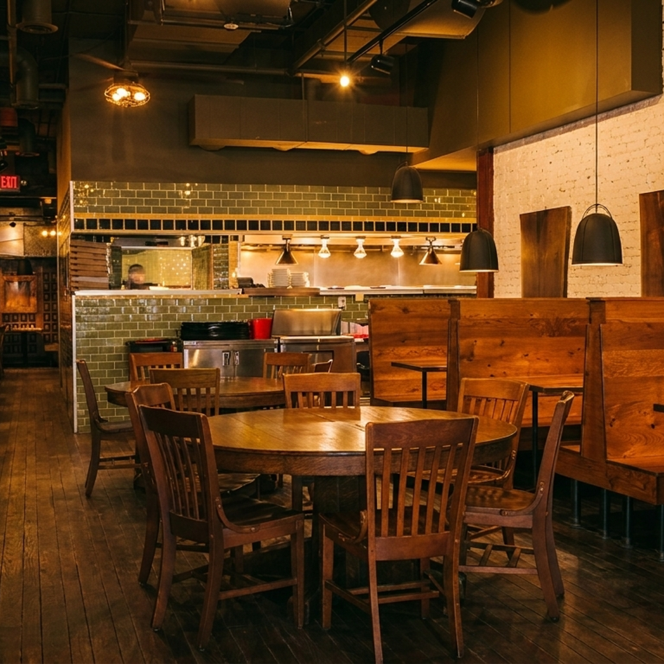 Warmly lit restaurant interior with wooden tables, booths, and an open kitchen with green tiled walls.